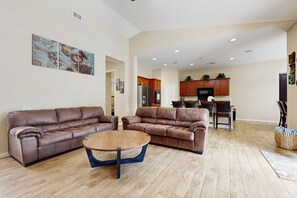 Ein geräumiges Wohnzimmer mit zwei braunen Ledersofas, einem Holztisch und einem Küchenbereich im Hintergrund.