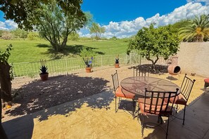 An outdoor patio with a round table and chairs, surrounded by potted plants and a view of a grassy field. - Classic and comfortable condo with pool, hot tub, & tennis (Tucson)