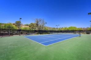 Una cancha de tenis con una red, rodeada por una valla y árboles.