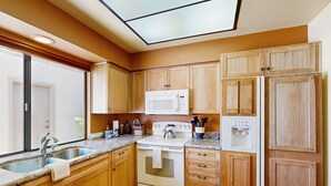 A kitchen with wooden cabinets, a white stove, a microwave, and a sink. - Classic and comfortable condo with pool, hot tub, & tennis (Tucson)