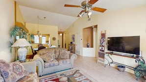 A living room with a sofa, TV, ceiling fan, and a dining area in the background. - Classic and comfortable condo with pool, hot tub, & tennis (Tucson)