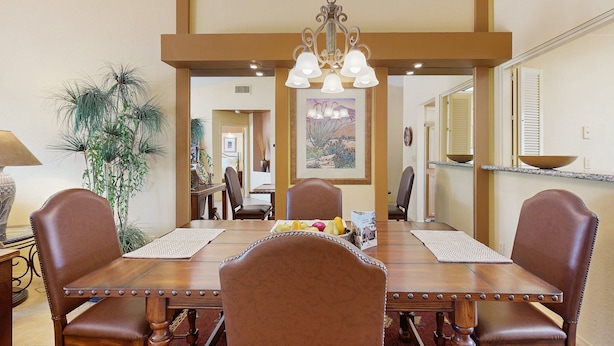 A dining area with a wooden table, six chairs, a chandelier, and a large mirror on the wall. - Classic and comfortable condo with pool, hot tub, & tennis (Tucson)