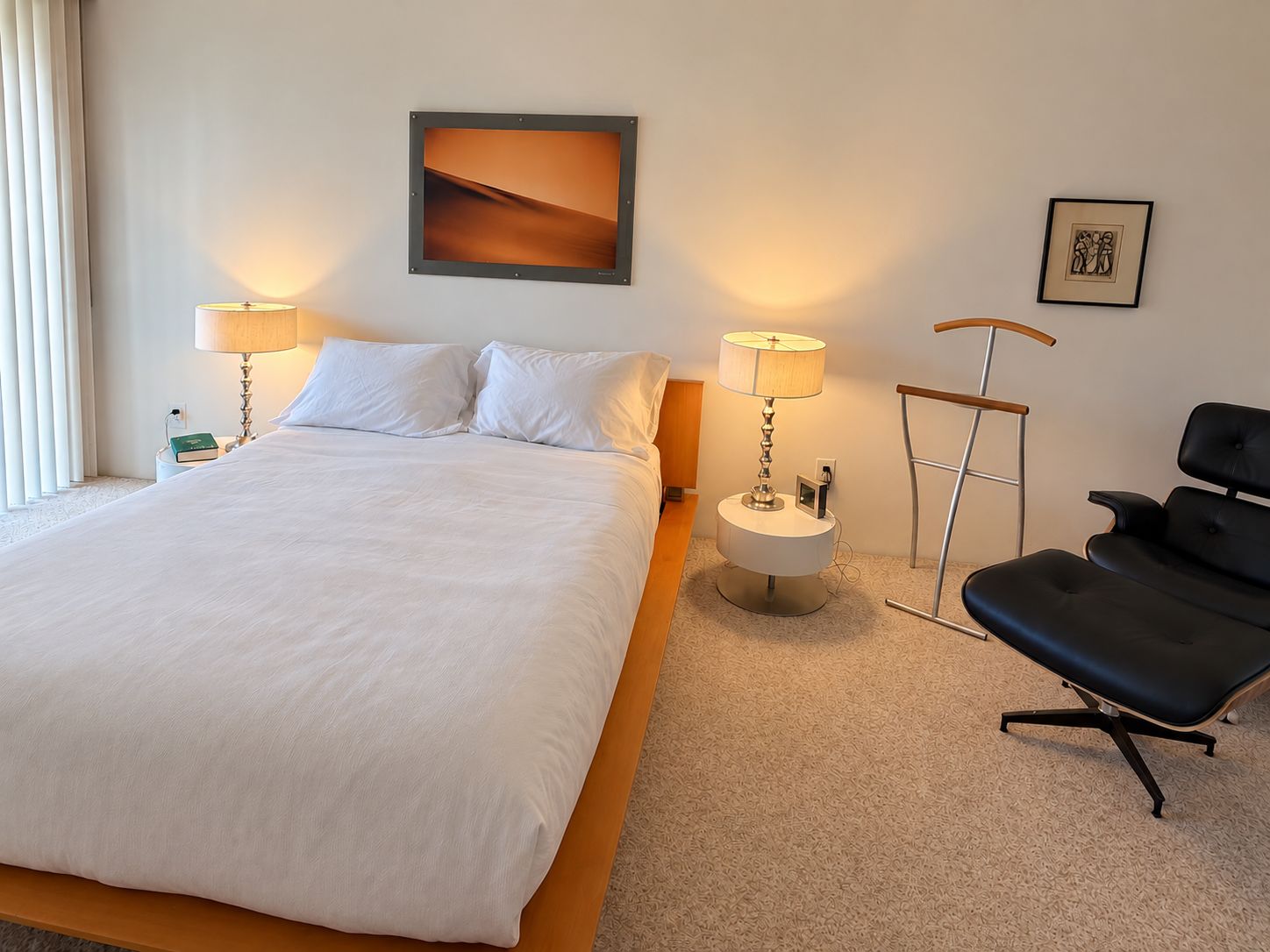 A hotel room with a large bed, two bedside lamps, a chair, a picture on the wall, and a small table with a book.