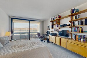 Une chambre d’hôtel avec un grand lit, un bureau avec un ordinateur, une bibliothèque et une vue sur l’extérieur.