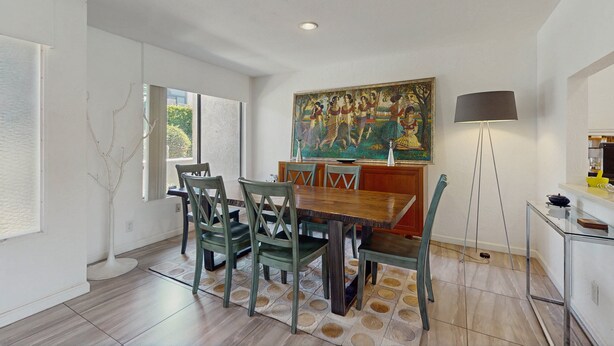 A dining area with a wooden table and chairs, a painting on the wall, a floor lamp, and a view of the outdoors. - Dog friendly condo w/two patios & shared pool/tennis - walk downtown (Palm Springs)
