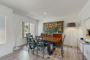 A dining area with a wooden table and chairs, a painting on the wall, a floor lamp, and a view of the outdoors. - Dog friendly condo w/two patios & shared pool/tennis - walk downtown (Palm Springs)