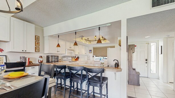 A modern kitchen with white cabinets, a central island with bar stools, pendant lighting, and a microwave. - Dog-Friendly Updated Condo Next to Golf Courses w/WiFi, AC, W/D, Shared Pool (Palm Desert)