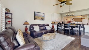 A modern living room with a brown leather sofa, a round coffee table, and a dining area with a white table and chairs. - Dog-Friendly Updated Condo Next to Golf Courses w/WiFi, AC, W/D, Shared Pool (Palm Desert)