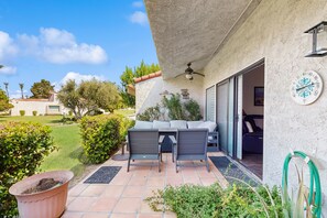 A patio with a table and chairs, a potted plant, and a hose on the wall. - Dog-Friendly Updated Condo Next to Golf Courses w/WiFi, AC, W/D, Shared Pool (Palm Desert)