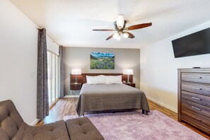 Une chambre à coucher avec un lit, des tables de chevet, une commode, un ventilateur de plafond et un tableau au mur.