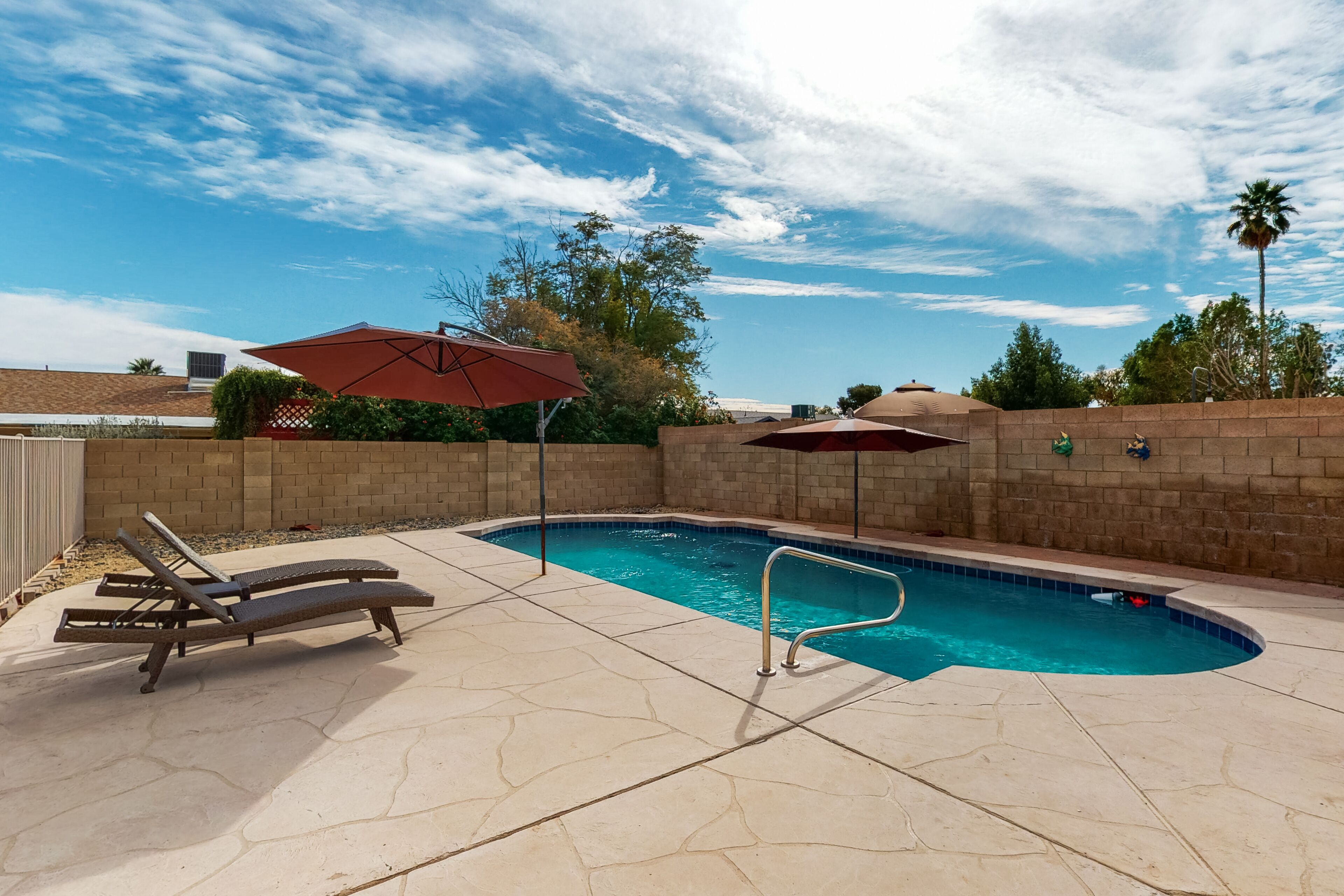 A swimming pool with lounge chairs and umbrellas, surrounded by a brick wall and trees.