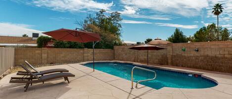 A swimming pool with lounge chairs and umbrellas, surrounded by a brick wall and trees.