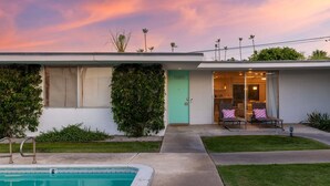 Una casa moderna con piscina, patio con mobili da esterno e una porta verde.