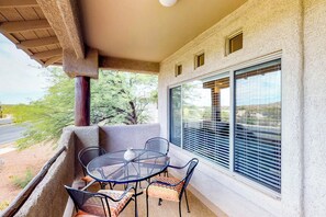 A balcony with a round table and chairs, a potted plant, and a view of a road and trees. - Spacious, dog-friendly condo with pool & hot tub (Oro Valley)