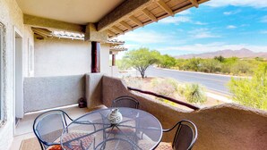 Un balcón con mesa y sillas, un jarrón decorativo y vistas a una carretera y un paisaje desértico.