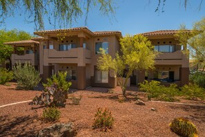 A multi-story building with a flat roof and a desert garden with cacti and small shrubs. - Spacious, dog-friendly condo with pool & hot tub (Oro Valley)