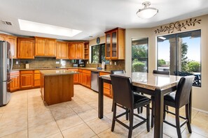 A modern kitchen with wooden cabinets, a central island, and a dining area with bar stools. - Tropical retreat with pool, grill, central air-conditioning, & washer/dryer (Phoenix)