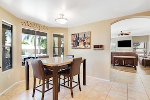 A dining area with a table and chairs, a painting on the wall, and a TV in the background. - Tropical retreat with pool, grill, central air-conditioning, & washer/dryer (Phoenix)