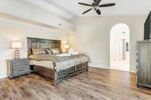 A bedroom with a wooden bed, nightstands, a ceiling fan, and an arched doorway leading to another room. - Tropical retreat with pool, grill, central air-conditioning, & washer/dryer (Phoenix)