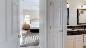 Habitación de hotel con cama, mesita de noche, lámpara y baño con lavamanos y espejo.