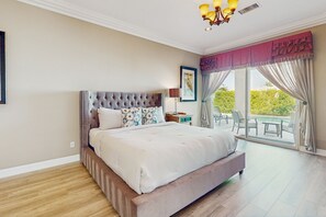 Ein geräumiges Schlafzimmer mit einem großen Bett, einem Nachttisch, einer Lampe und Blick ins Freie durch eine Glastür.