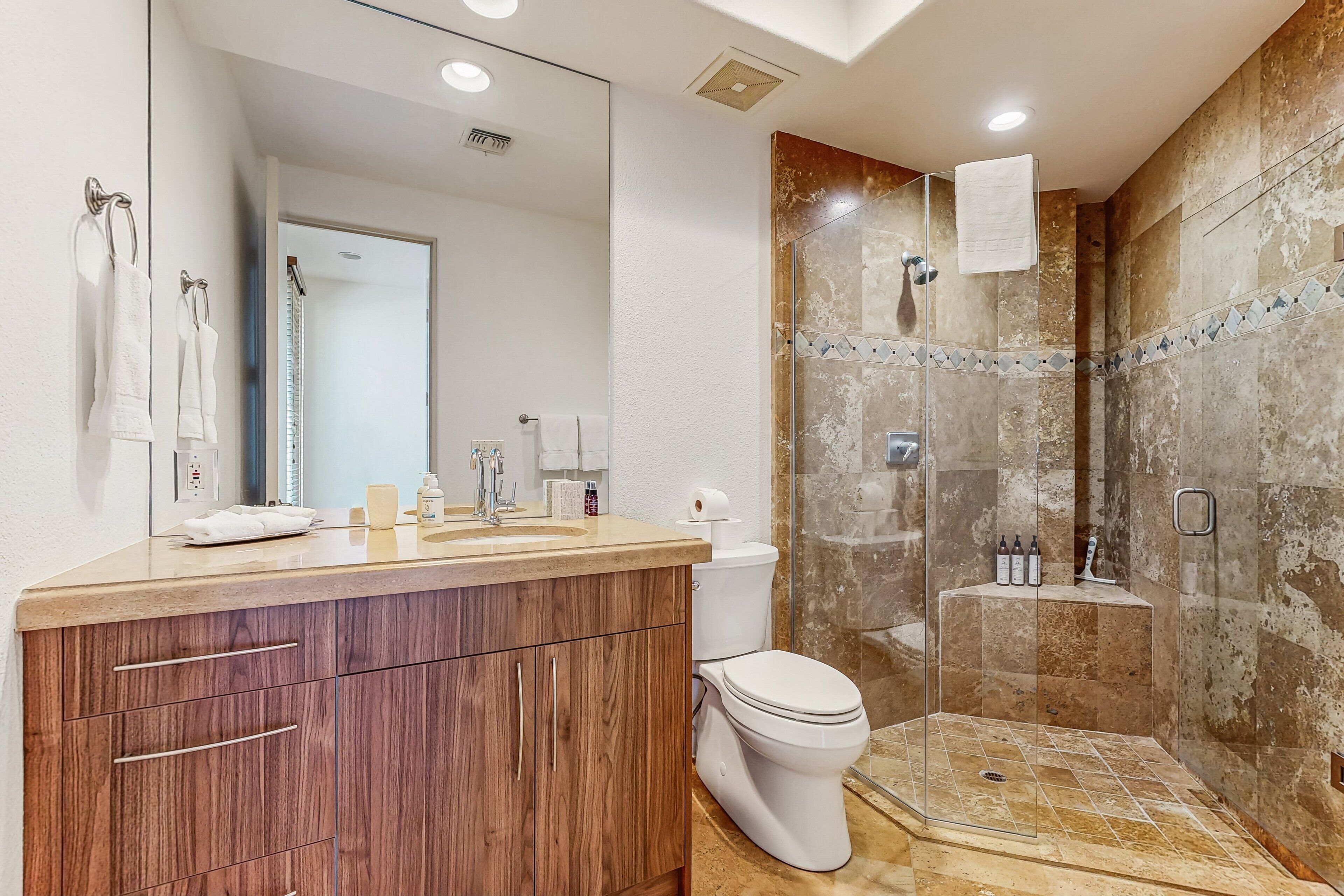 Un baño moderno con tocador de madera, cabina de ducha de vidrio y inodoro blanco.