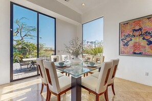 A dining area with a glass table, white chairs, and a vase of flowers. - Lakeside luxury home w/ private pool & spa, fireplace & outdoor kitchen-dog ok (La Quinta)