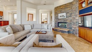 A modern living room with a sectional sofa, a fireplace, and a stone accent wall. - Lakeside luxury home w/ private pool & spa, fireplace & outdoor kitchen-dog ok (La Quinta)