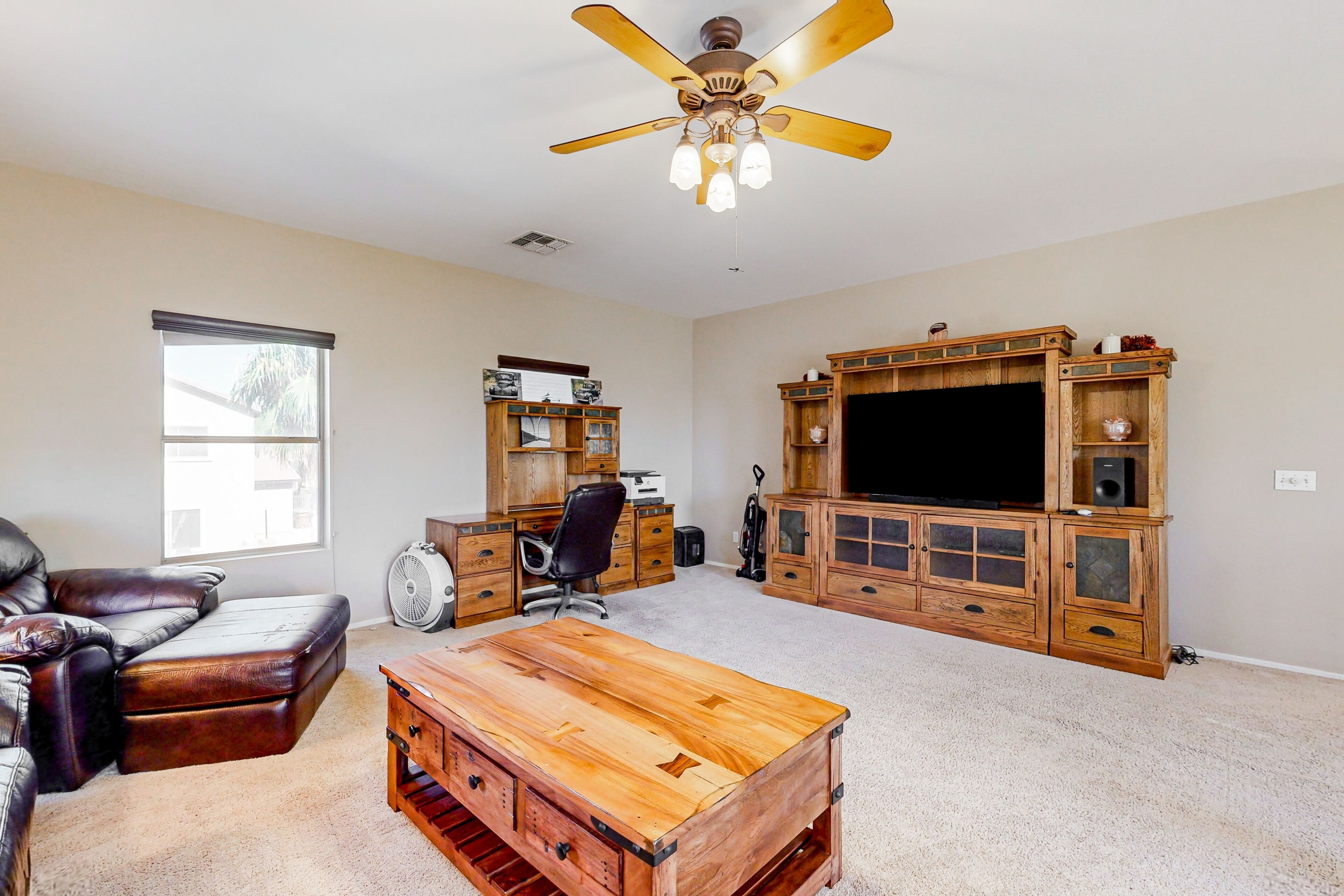 A spacious living room with a ceiling fan, a leather couch, a wooden coffee table, and a television set on a wooden cabinet.