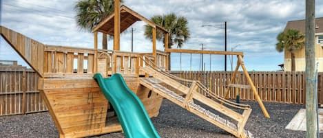 Une structure de jeu en bois comprenant un toboggan, des escaliers et une petite extension en forme de maison.