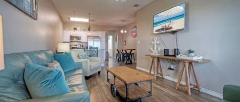 A living room with a sofa, a coffee table, a TV, and a kitchen in the background.