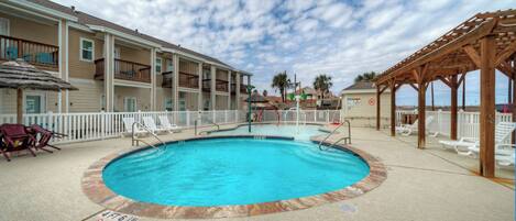 A swimming pool with a deck, lounge chairs, and a wooden pergola.