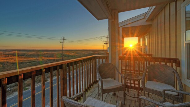 A wooden deck with wicker chairs and a view of the sunset over a flat landscape. - Ocean's 96 by Avantstay Heated Pool + Foosball Table + Media Room + Walk to North Padre Beach (Corpus Christi)