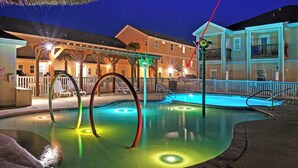 A swimming pool with a deck, a covered area with chairs, and a building with a balcony in the background. - Ocean's 96 by Avantstay Heated Pool + Foosball Table + Media Room + Walk to North Padre Beach (Corpus Christi)