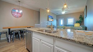 A kitchen with granite countertops, a dishwasher, and a dining area with chairs and a table. - Ocean's 96 by Avantstay Heated Pool + Foosball Table + Media Room + Walk to North Padre Beach (Corpus Christi)