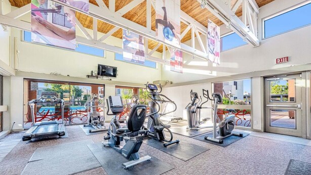 A gym with cardio machines, weight stations, and a large window overlooking a pool. - Golf-course-front condo near Old Town with two patios, WiFi, pool & hot tub (Scottsdale)