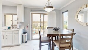 A dining area with a table, chairs, a chandelier, a trash can, and a view through a sliding glass door. - Golf-course-front condo near Old Town with two patios, WiFi, pool & hot tub (Scottsdale)