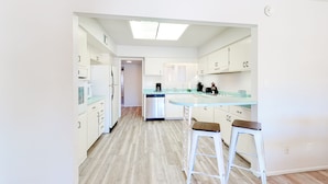 Una cucina moderna con mobili bianchi, un'isola centrale con sgabelli e una lavastoviglie.
