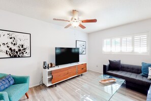 A modern living room with a flat-screen TV, wooden cabinet, glass coffee table, and two sofas. - Dog-friendly house with retro feel, pool, fireplace & patio - snowbirds welcome (Scottsdale)