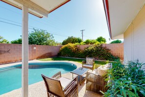 A backyard with a swimming pool, wicker furniture, and a brick wall. - Dog-friendly house with retro feel, pool, fireplace & patio - snowbirds welcome (Scottsdale)