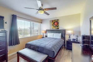 Une chambre d’hôtel comprenant un lit, des tables de chevet, un bureau, un ventilateur de plafond et une fenêtre avec des stores.