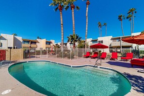 A swimming pool with clear water, surrounded by palm trees and red lounge chairs. - Sun-filled condo with a patio, central AC, pool & grill access - great location (Scottsdale)