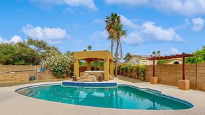 A swimming pool with a pergola and a rock feature, surrounded by a brick wall and greenery. - Scottsdale Style Meets Family-Friendly Fun! Spacious home with a yard and pool. (Scottsdale)