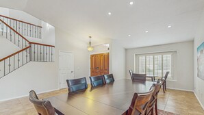 A spacious dining area with a large wooden table and six chairs, a staircase with wooden railings, and a door leading to another room. - Scottsdale Style Meets Family-Friendly Fun! Spacious home with a yard and pool. (Scottsdale)