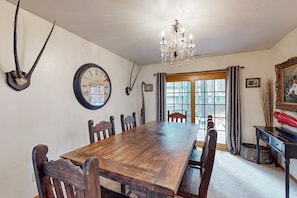 A dining room with a wooden table, chairs, a chandelier, a clock, and a window with curtains. - Lavish retreat with game room, tranquil porch & scenic yard-near skiing & dining (Flagstaff)