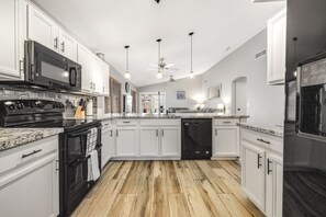 A modern kitchen with white cabinets, granite countertops, a black stove, and a black dishwasher. - Sunny & stylish home with private pool, central AC, W/D & firepit (Glendale)