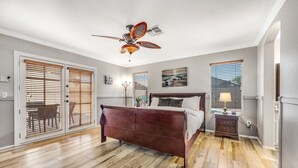 Een slaapkamer met houten vloer, een bed met hoofdeinde, een plafondventilator en een nachtkastje met lamp.