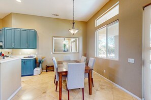 A dining area with a wooden table and chairs, a kitchen with teal cabinets, and a large window providing natural light. - Dog-Friendly Golfer's Haven w/Private Pool & Spa - On 6th Hole of Dunes Course (La Quinta)