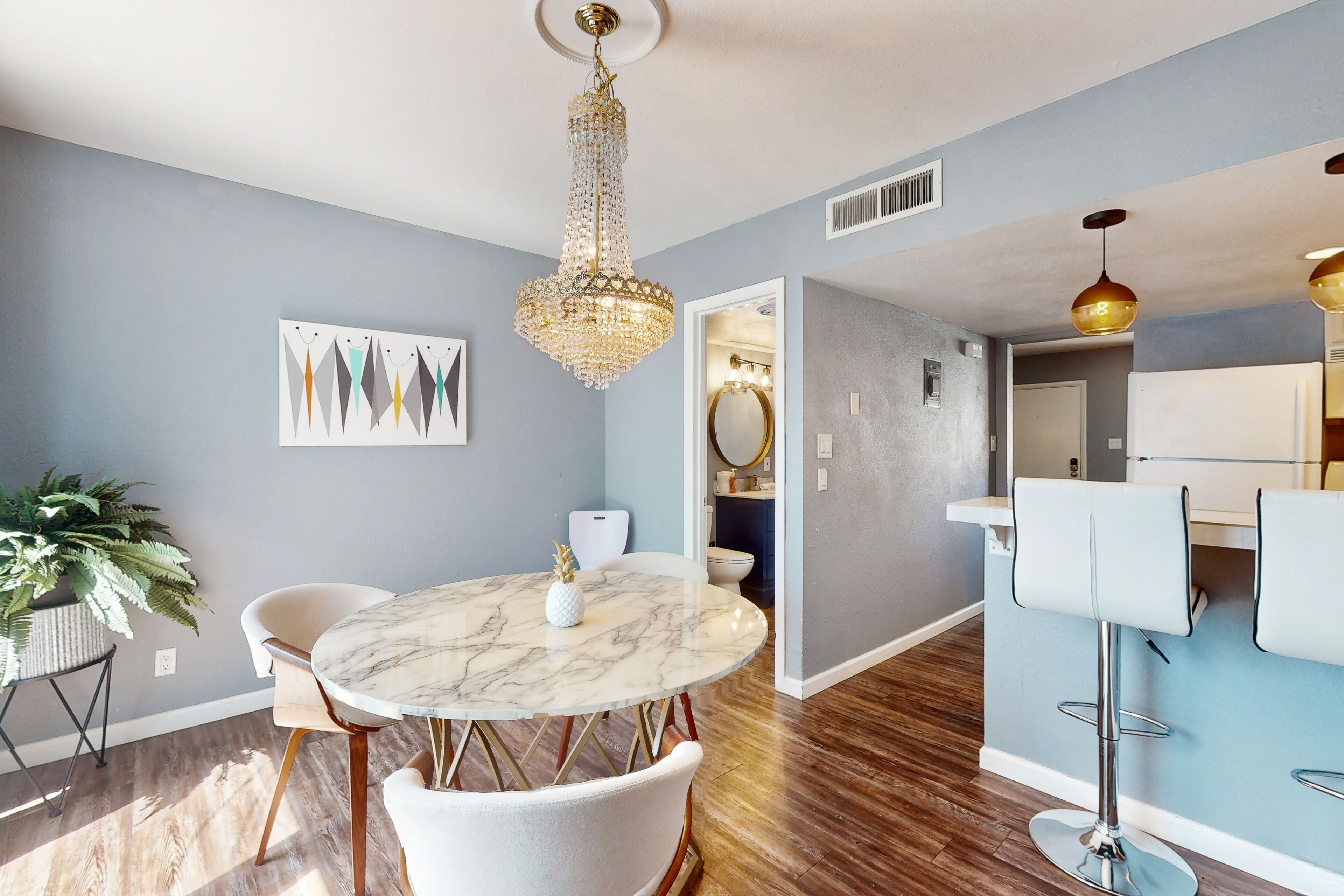 A modern dining area with a marble table, white chairs, and a chandelier.
