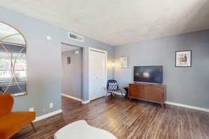 A modern living room with hardwood flooring, a television, a wooden cabinet, and a chair. - Snowbird-Friendly Condo with Patio Access, Central AC, Free WiFi - Dogs Welcome (Glendale)